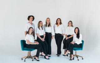 Team of women, some sitting on teal velvet chairs.