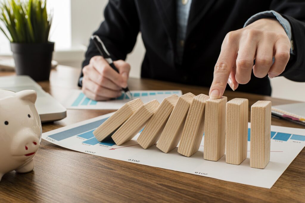 Business women stopping dominoes falling that are sitting on top of underinsurance paperwork on desk