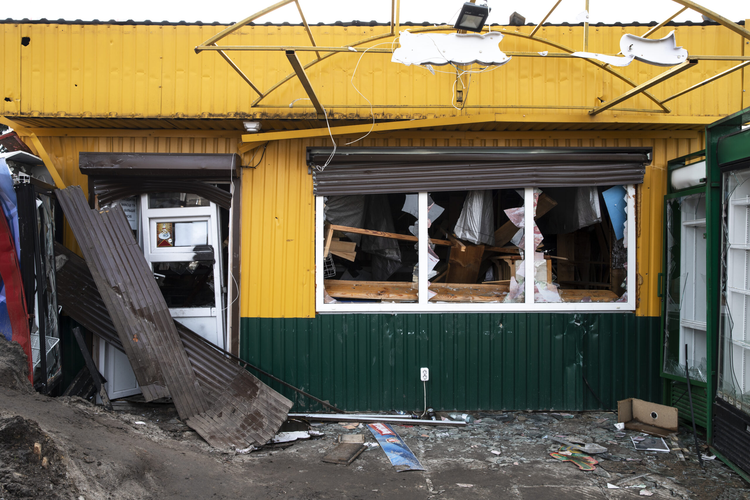 Damaged underinsured yellow and green shop, with broken windows, twisted iron, glass on ground